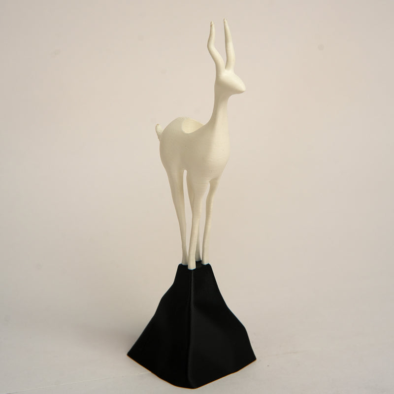 White deer figurine on a black stand against a beige background
