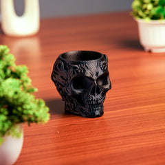 Black skull-shaped vase on a wooden surface with plants in the background