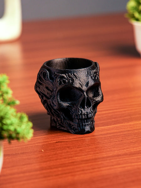 Black skull-shaped vase on a wooden surface with plants in the background