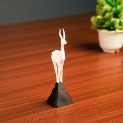 White deer figurine on a black base on a wooden surface with a blurred plant in the background