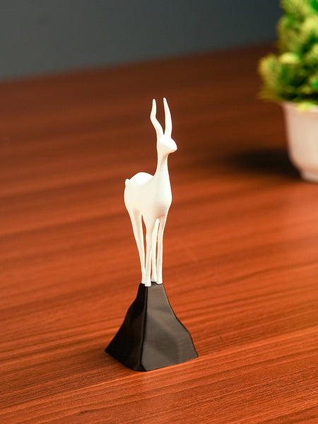White deer figurine on a black base on a wooden surface with a blurred plant in the background