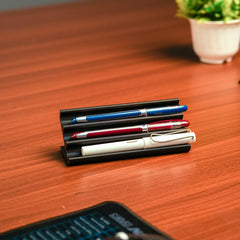 Set of pens in a holder on a wooden desk with a plant in the background