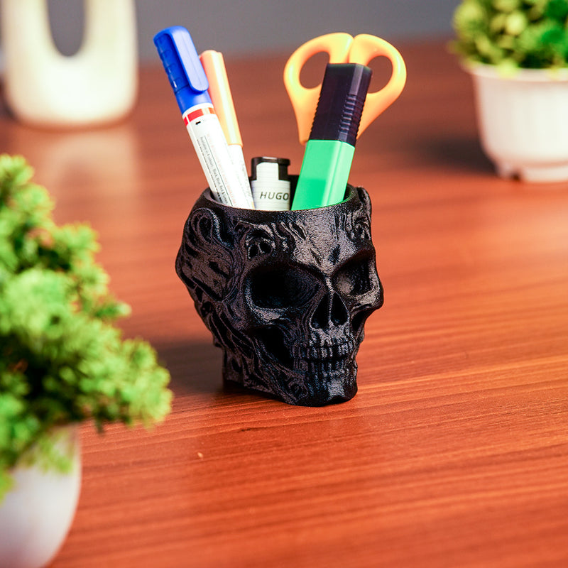 Black skull-shaped pen holder with stationery items on a wooden surface
