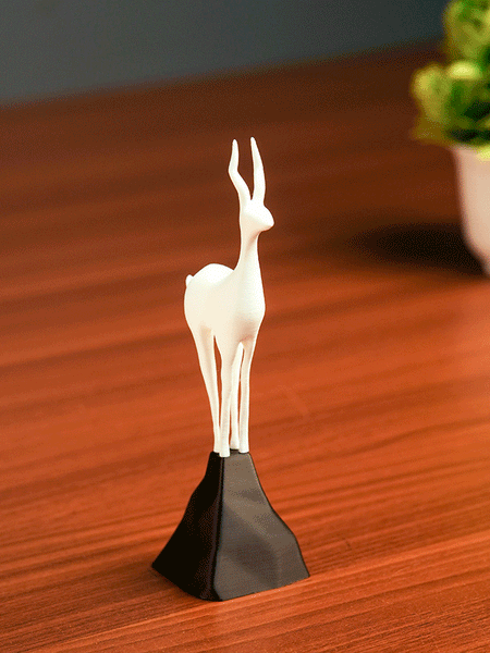 White deer figurine on a black stand against a beige background